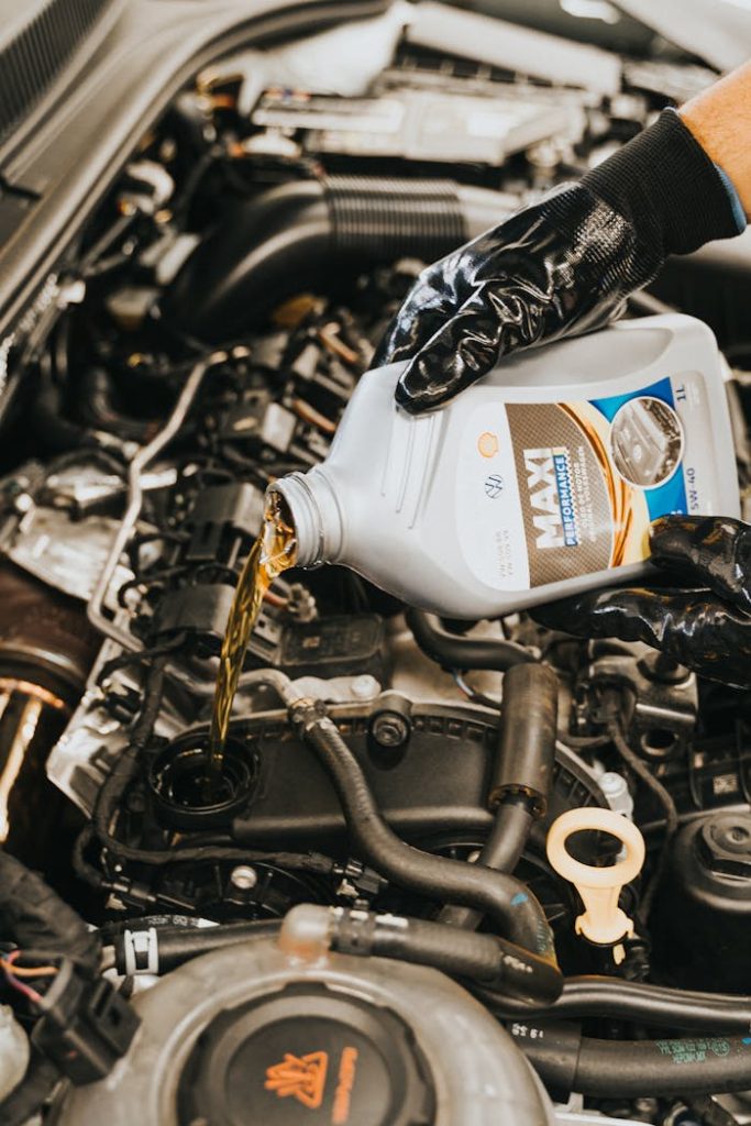 hand-pouring-oil-to-engine-13065699 Close-up of mechanic pouring engine oil into car engine with gloved hands, showcasing automotive maintenance.