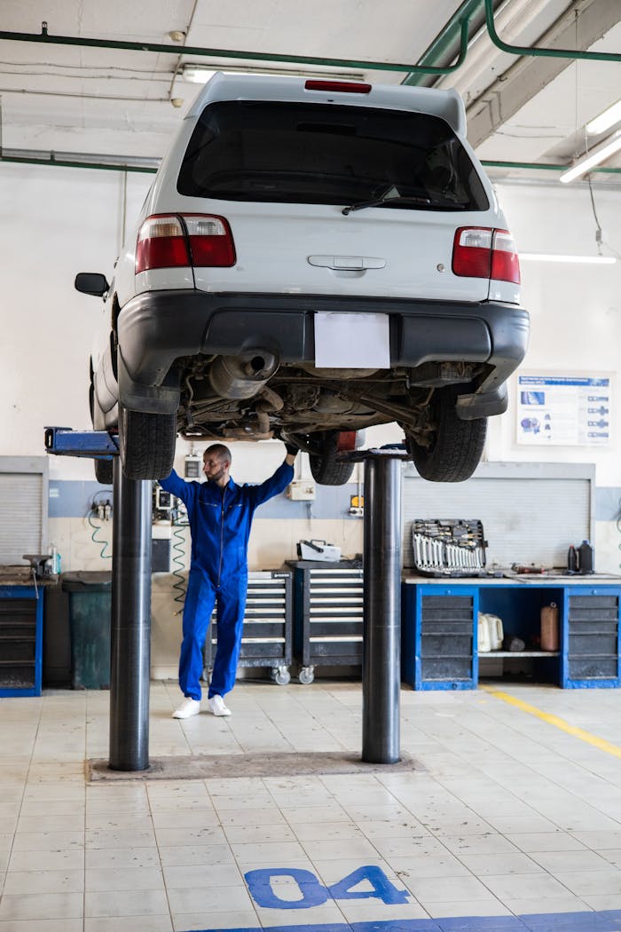 services-02 Mechanic in blue coverall inspecting a lifted car in an auto repair shop.